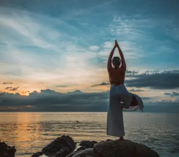 Frau in einer Yoga-Stellung auf einem Stein und mit Blick auf das Meer